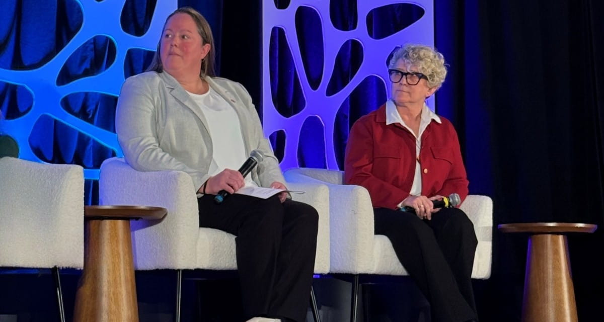 Laurie Swami and Jennifer Lennox from NB Power are sitting in white armchairs holding microphones onstage at the Women in Nuclear conference