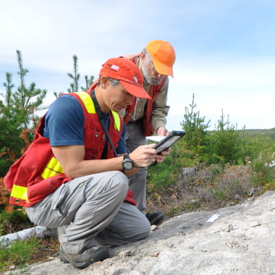 A photo of NWMO geologists outdoors examining rock and making notes