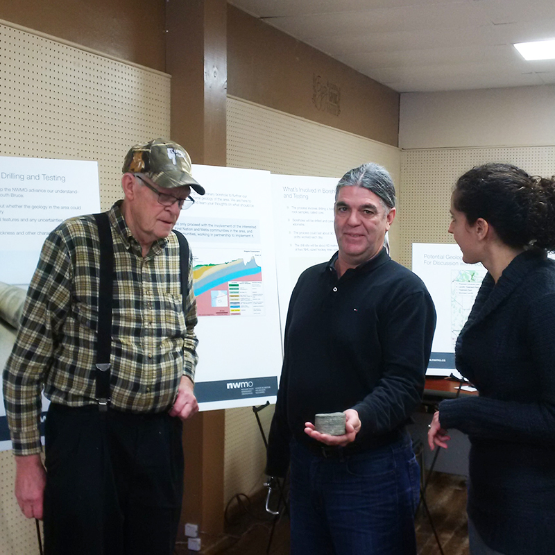 This picture shows a South Bruce man examining a piece of rock core while taking to NWMO staff about borehole drilling at an open house in Teeswater.