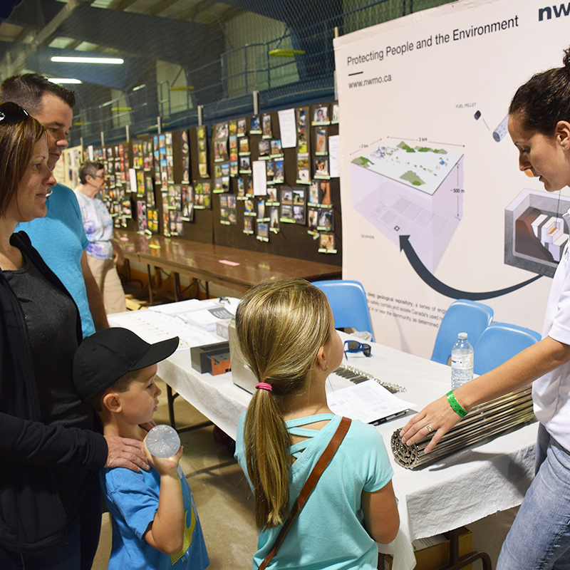 Cette photo montre une famille apprenant davantage sur le combustible nucléaire irradié auprès de Cherie Leslie de la SGDN lors de la foire de Teeswater.