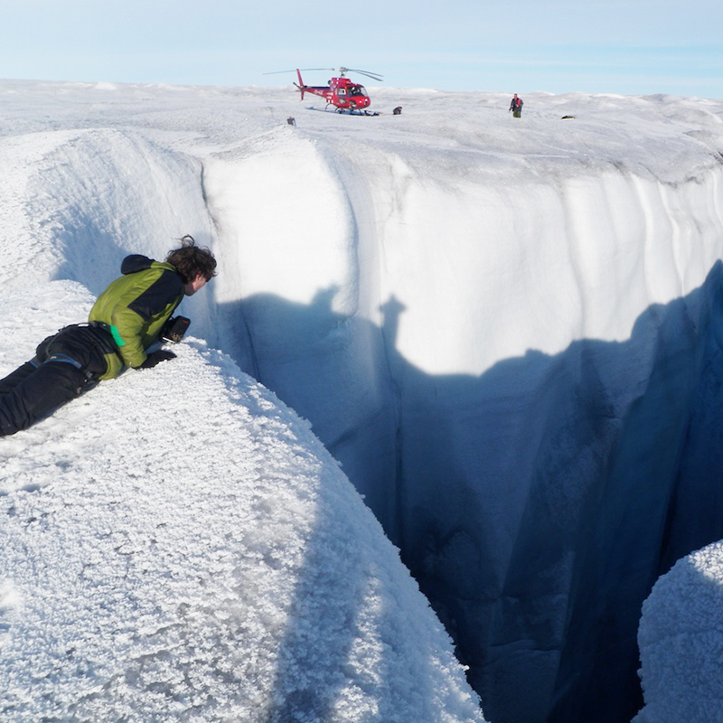 This image shows researchers and scientists observing features on the Greenland Ice Sheet to contribute to the Greenland Analogue Project with a helicopter in the background.