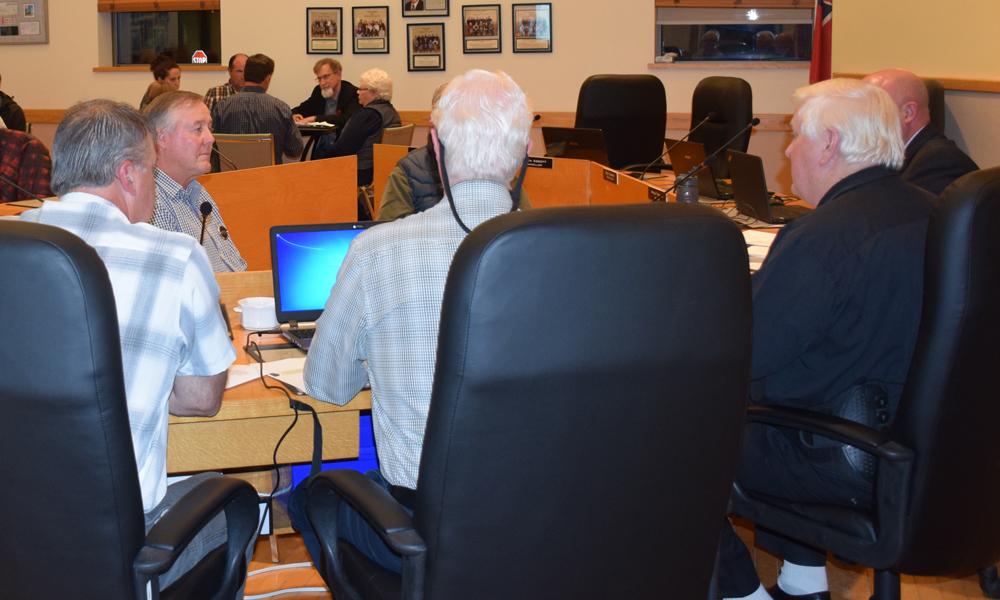 Image shows six people sitting at a table, with another five people sitting at a different table in the distance.