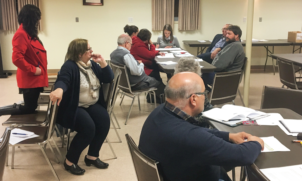 This photo shows members of  the South Bruce Council and Community Liaison Committee, and members of the public at two tables discussing and considering values and principles to guide more detailed  conversations around partnership.
