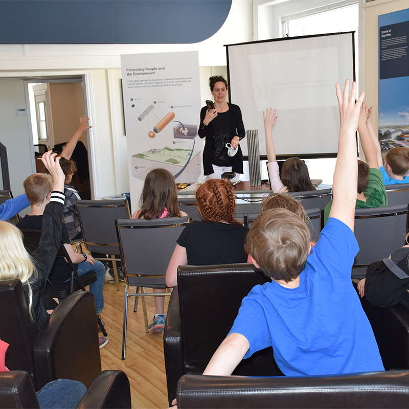 This picture depicts an NWMO employee engaging a Grade4/5 class of school children in an interactive presentation about radiation.