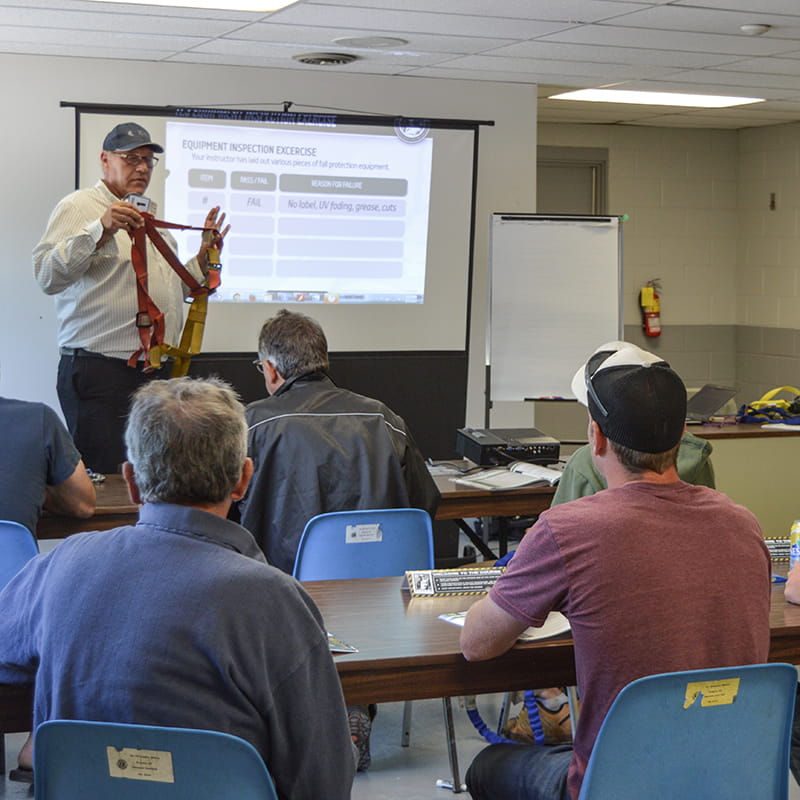The photo shows an instructor showing a group of students how to properly wear a harness as part of a Working at Heights class offered in South Bruce.