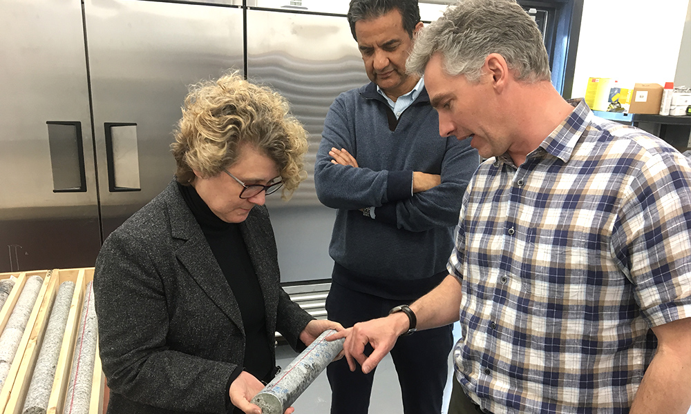 Image shows three people examining a core sample from a borehole. 