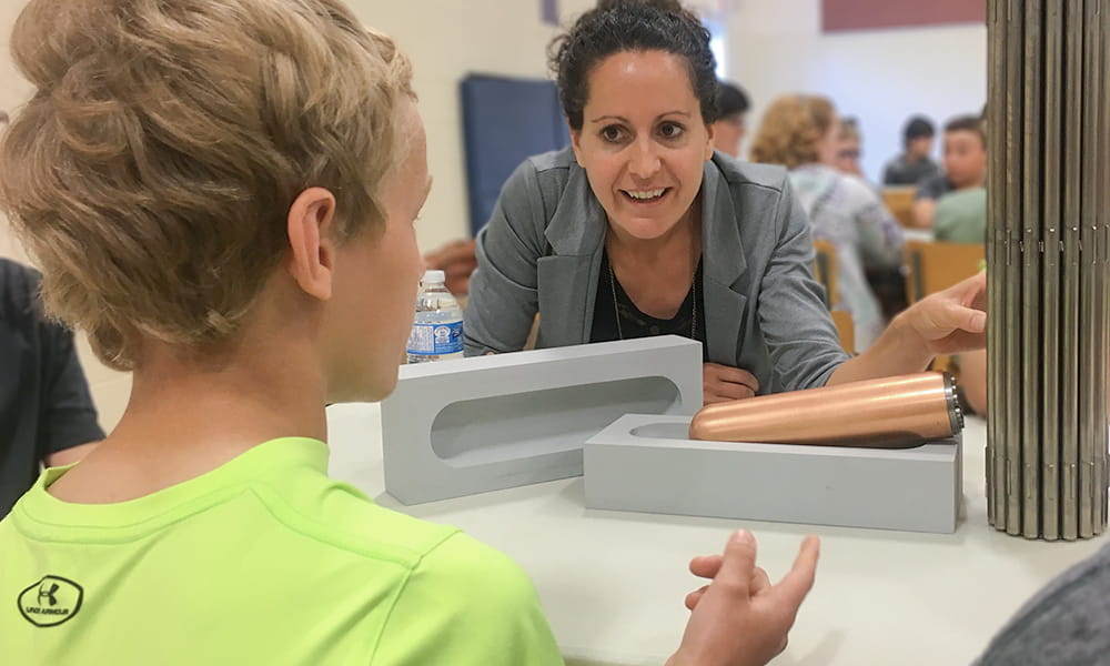 Photo shows a woman listening to a student speak; the student has his back to the camera.