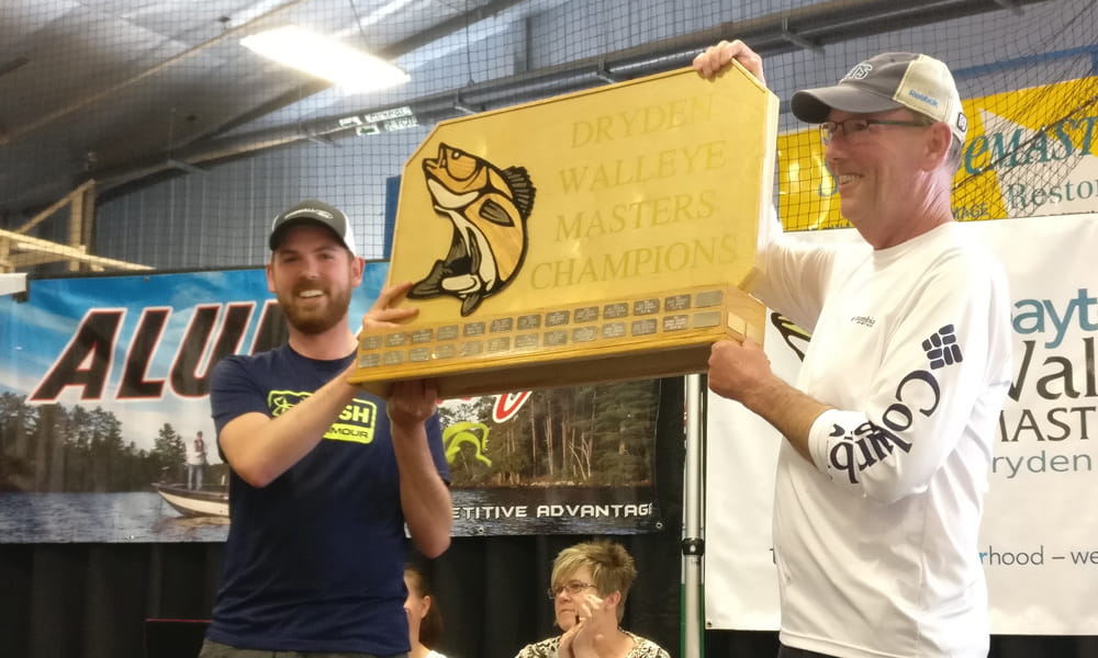 Image shows two men holding up a prize in the form of a plaque.