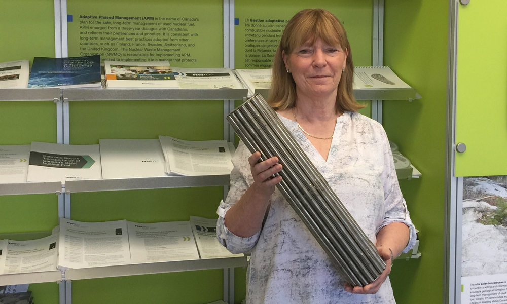 Photo shows a woman holding up an empty used nuclear fuel bundle.