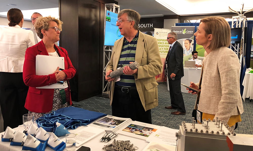 Image shows three people chatting near a table at a convention booth. 
