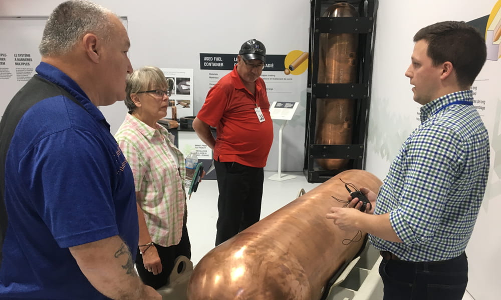 Image shows four people talking around a copper container. 