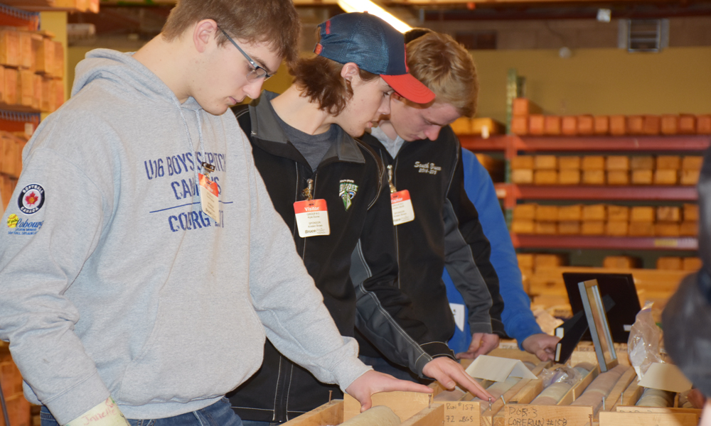 A row of students look at rock core samples on a table. 