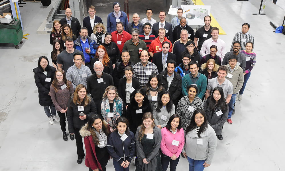 Photo shows a large group of people standing in an indoor space.