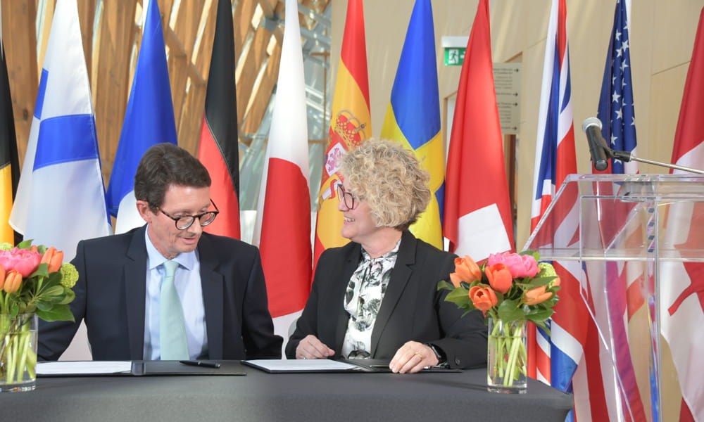 Two people seated at a table preparing to sign papers. 