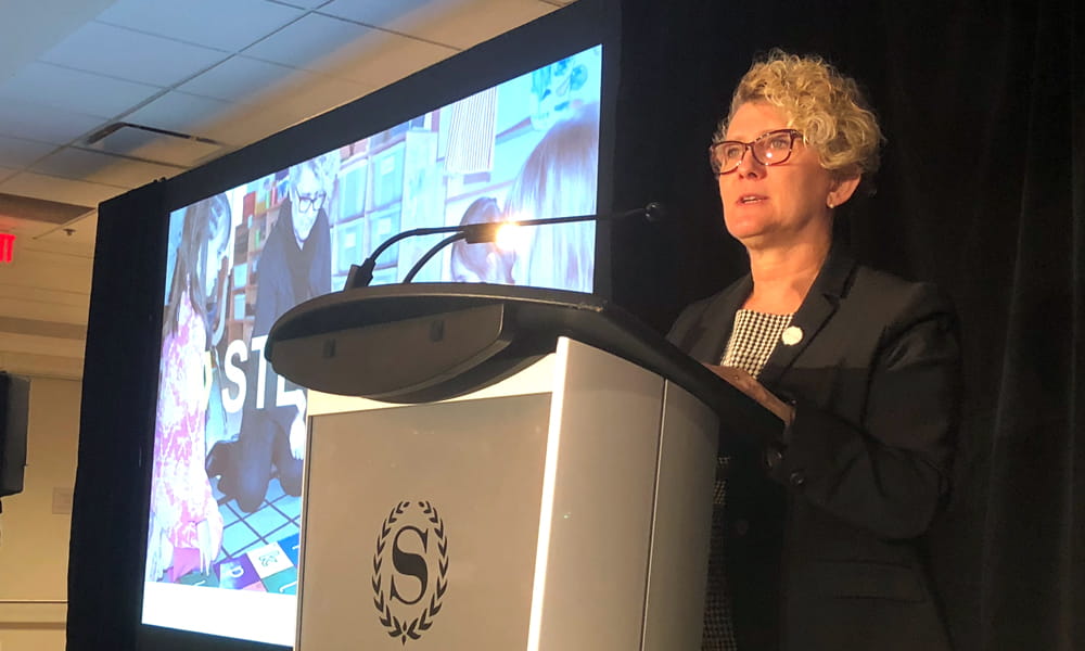 La photo montre une femme parlant derrière un podium.