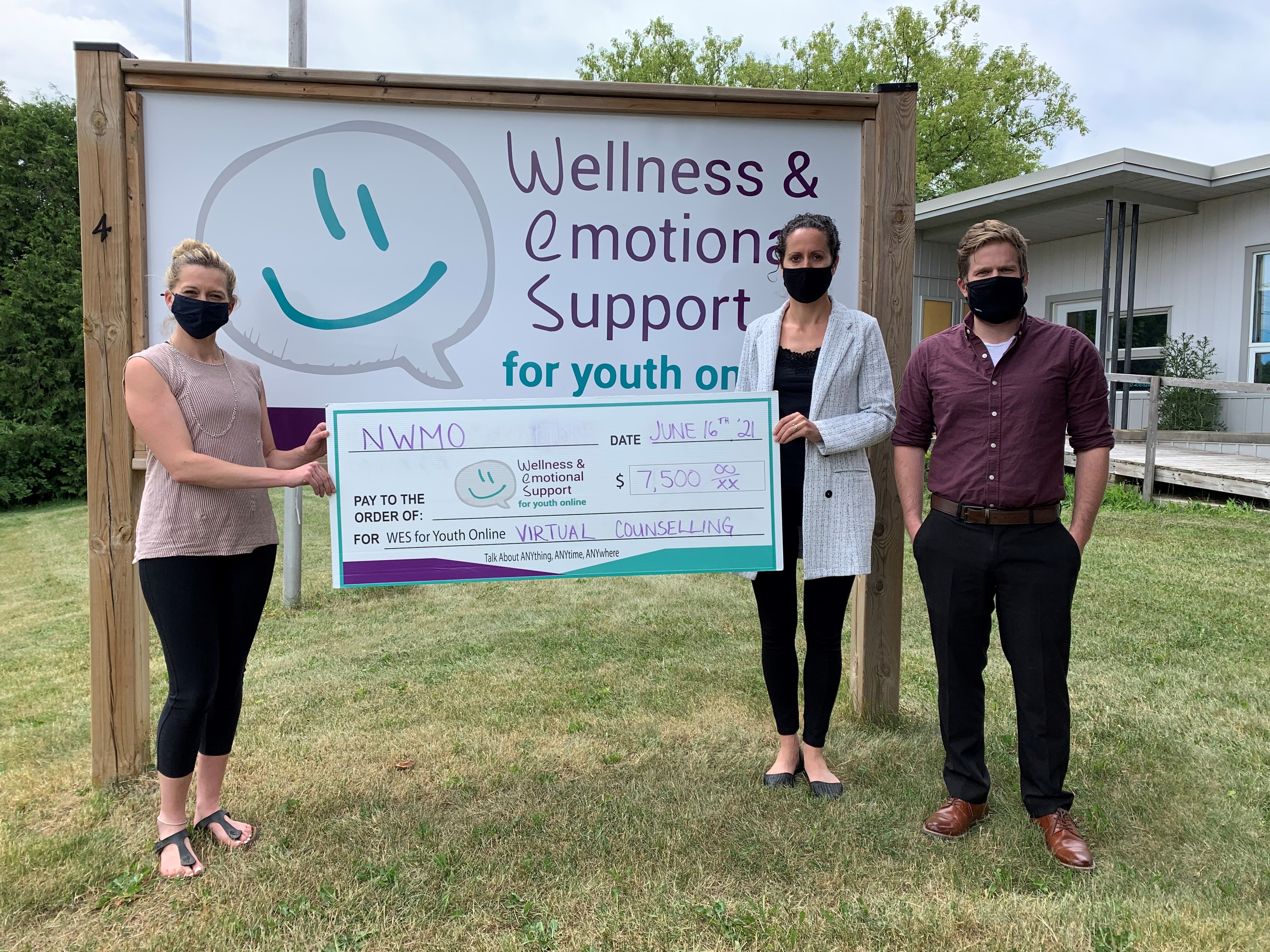 Two NWMO employees handing a large cheque to a WES for Youth Online employee. Everyone is wearing a mask.