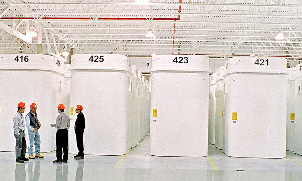 La photo montre des conteneurs de stockage à sec en arrière-plan et quatre individus vêtus de casques de sécurité  l’avant plan.