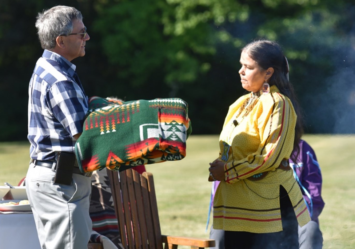 An individual handing a blanket to an Indigenous Elder.