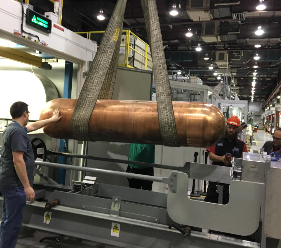 Used fuel container being loaded into a machine that rotates the container for the cold spray copper process.