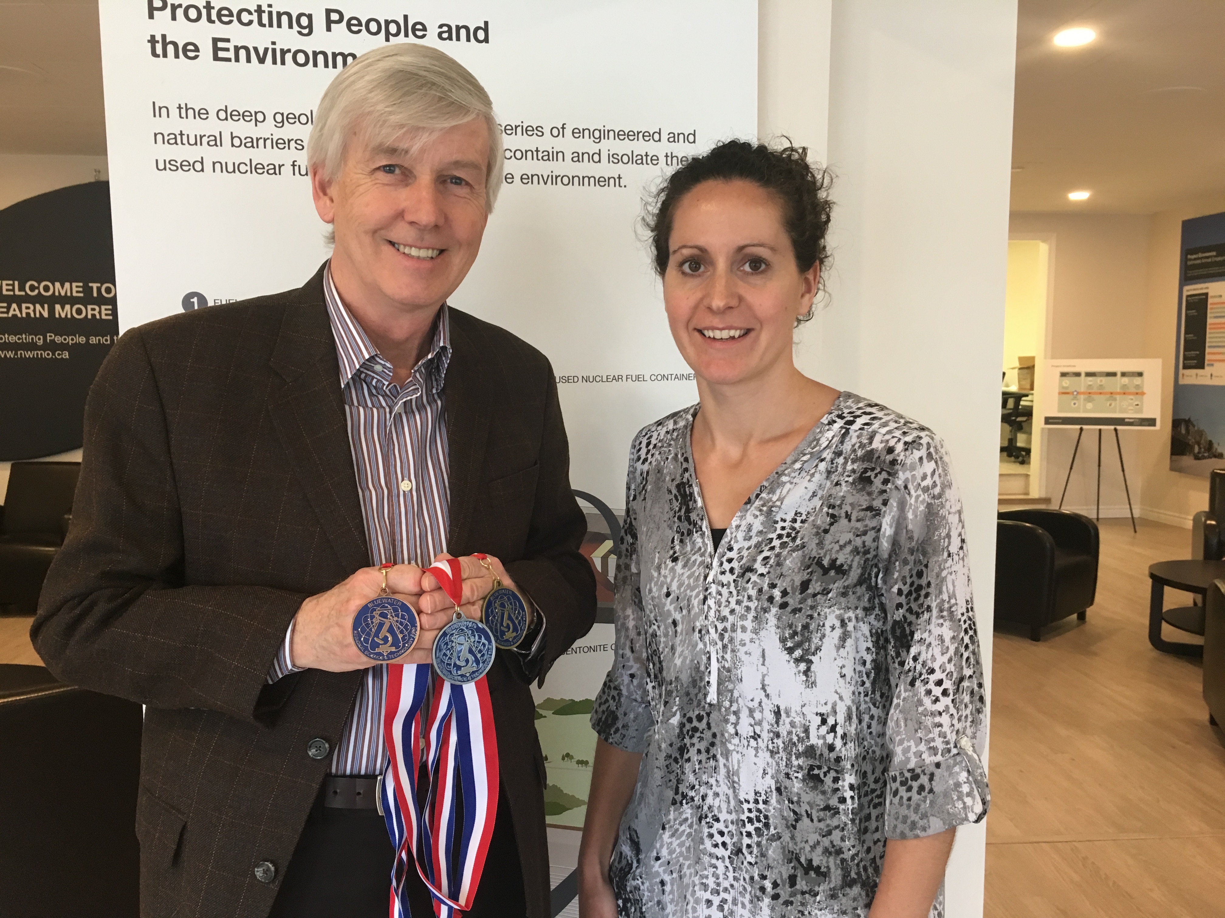 Peter Thor, Treasurer for the Bluewater Regional Science and Technology Fair, shows off the student medals for the upcoming science fair with Cherie Leslie, Senior Engagement Advisor for the NWMO and volunteer judge for the event.