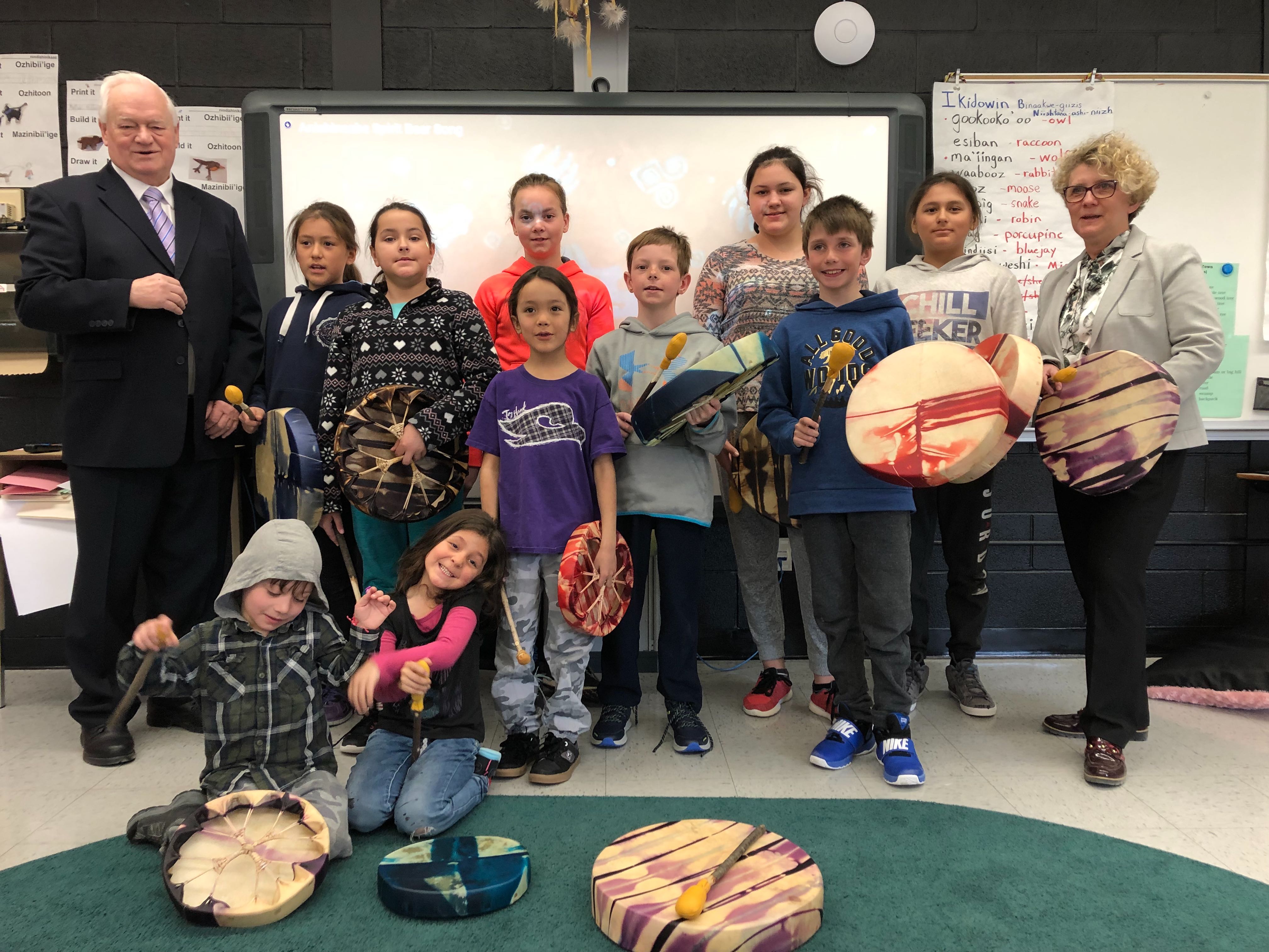 John MacEachern (left), Mayor of Manitouwadge, and Laurie Swami (right), President and CEO of the NWMO, visit a classroom at Our Lady of Lourdes Catholic School, where an NWMO investment has helped support the purchase of traditional drums.