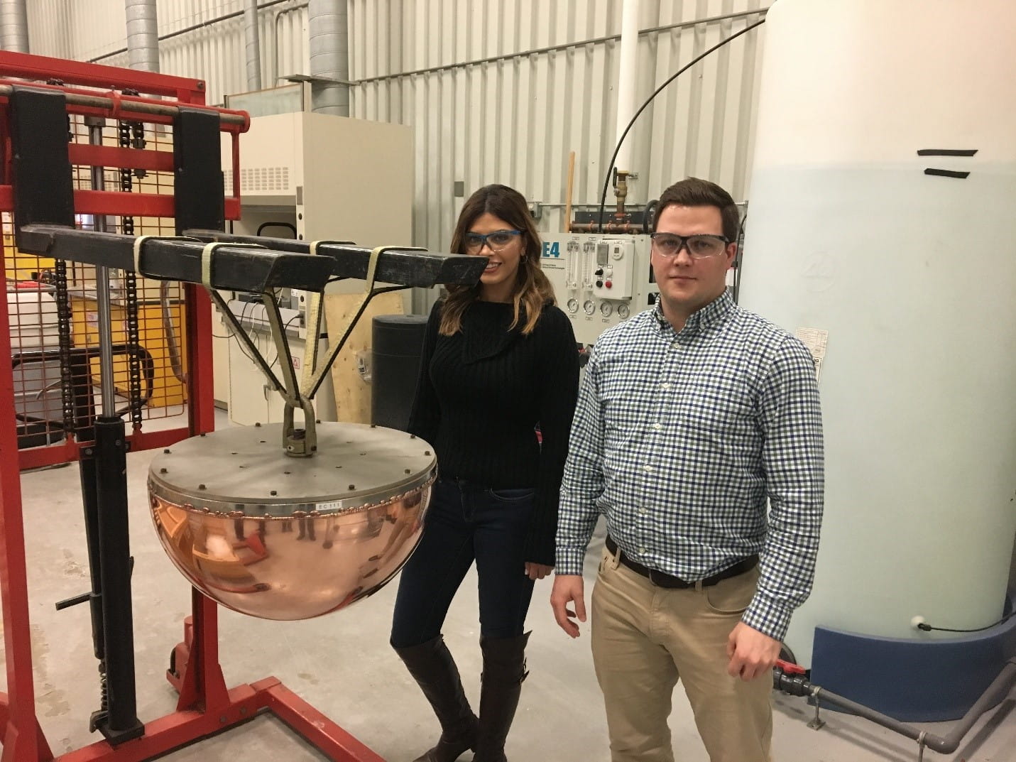 Scientists standing next to section of a prototype of the copper-coated used nuclear fuel container